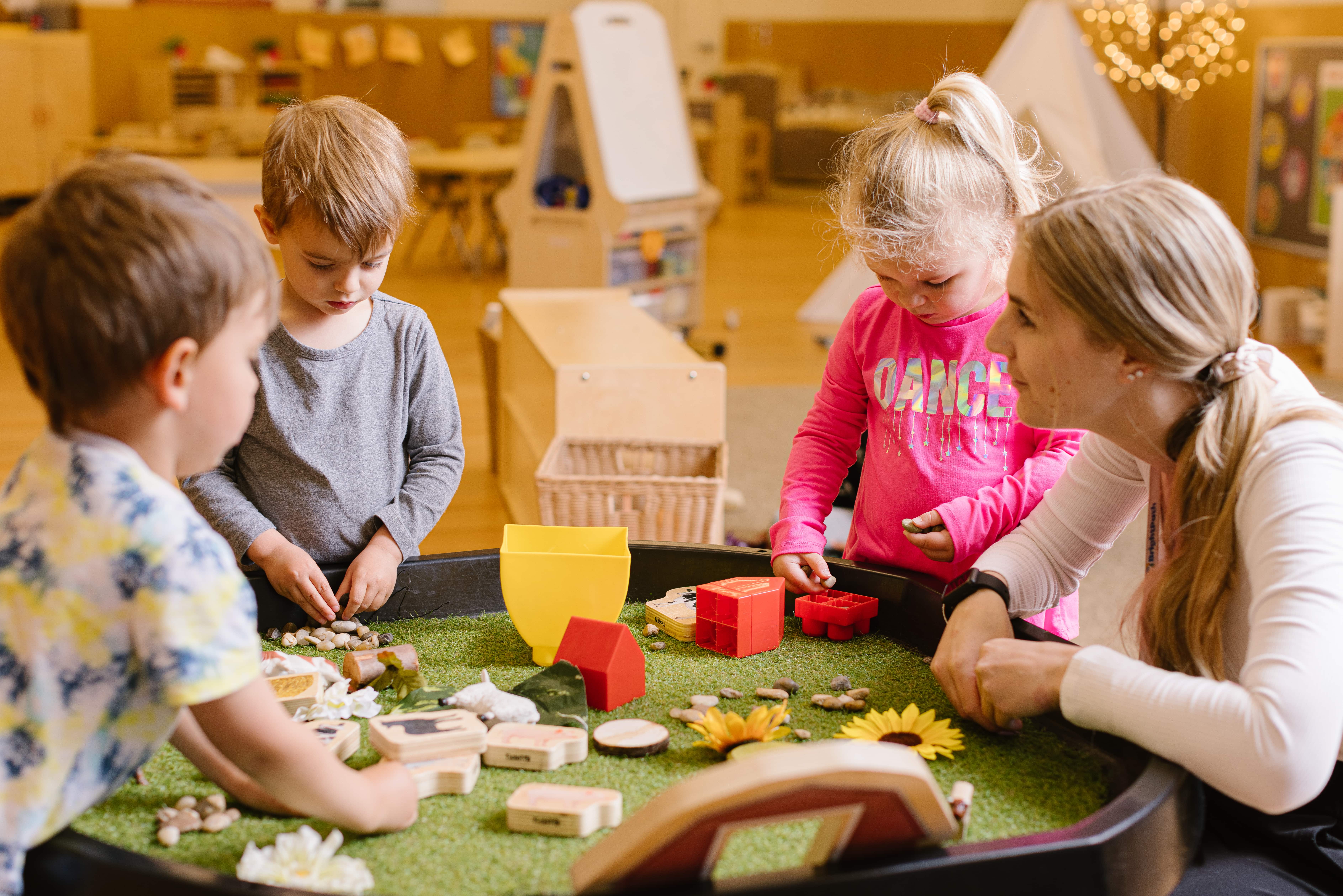 A BrightPath Child Care Center educator sitting with children around a sensory table while the children are learning through play. 