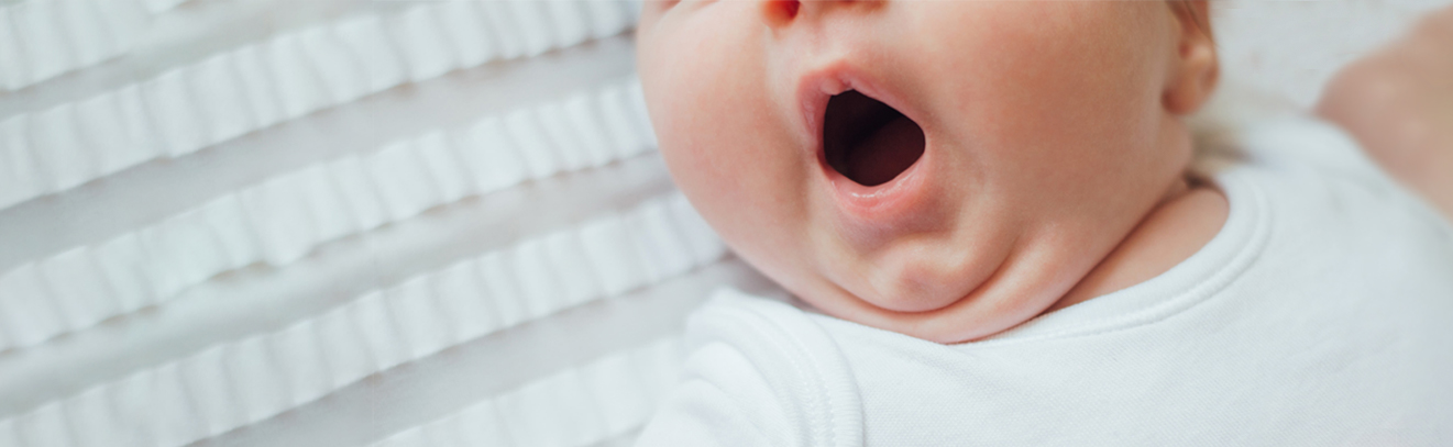 An infant yawning in bed as parents learn how to get sleep back on track!