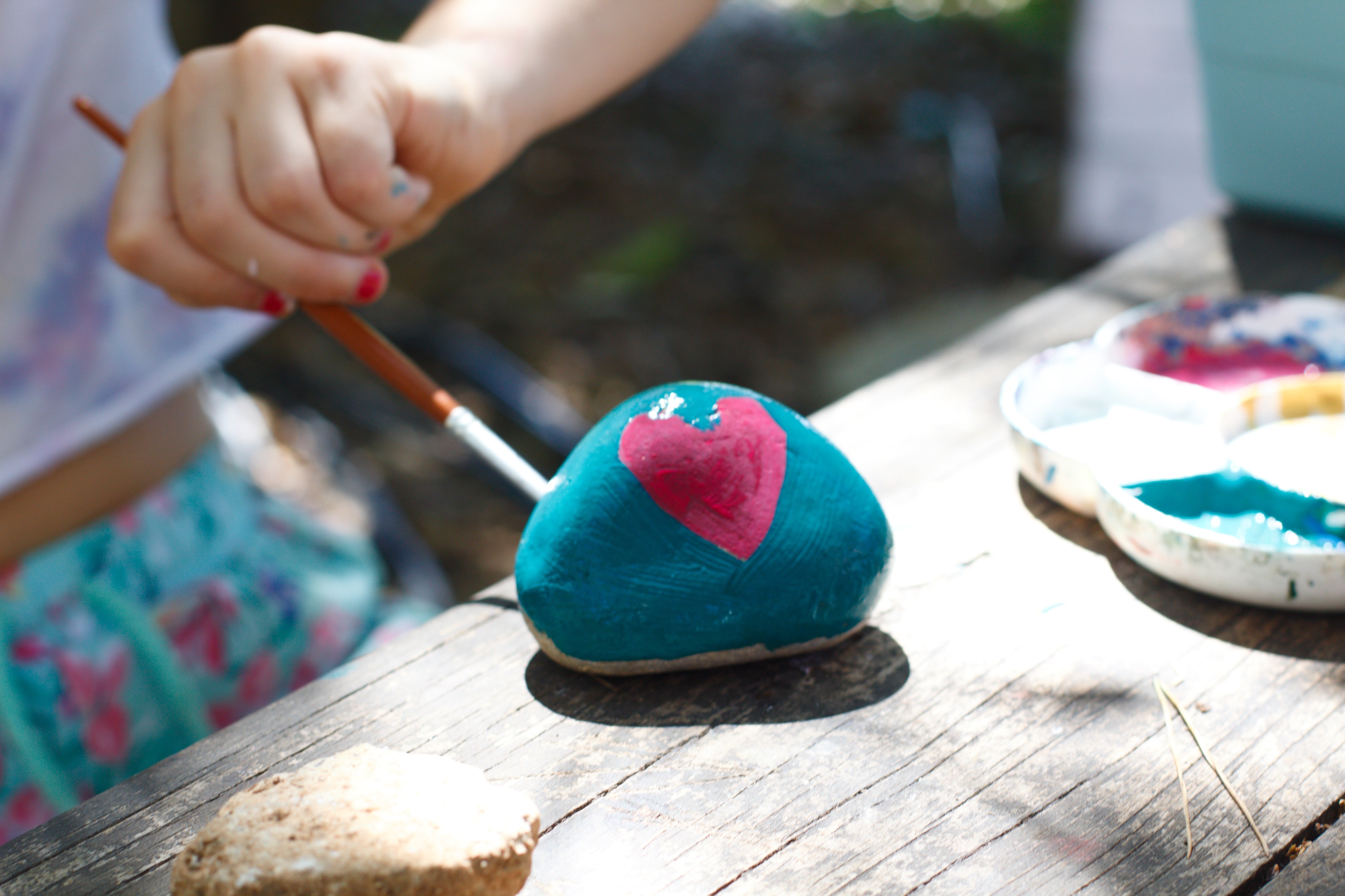 Little girl painting rock blue with a pink heart