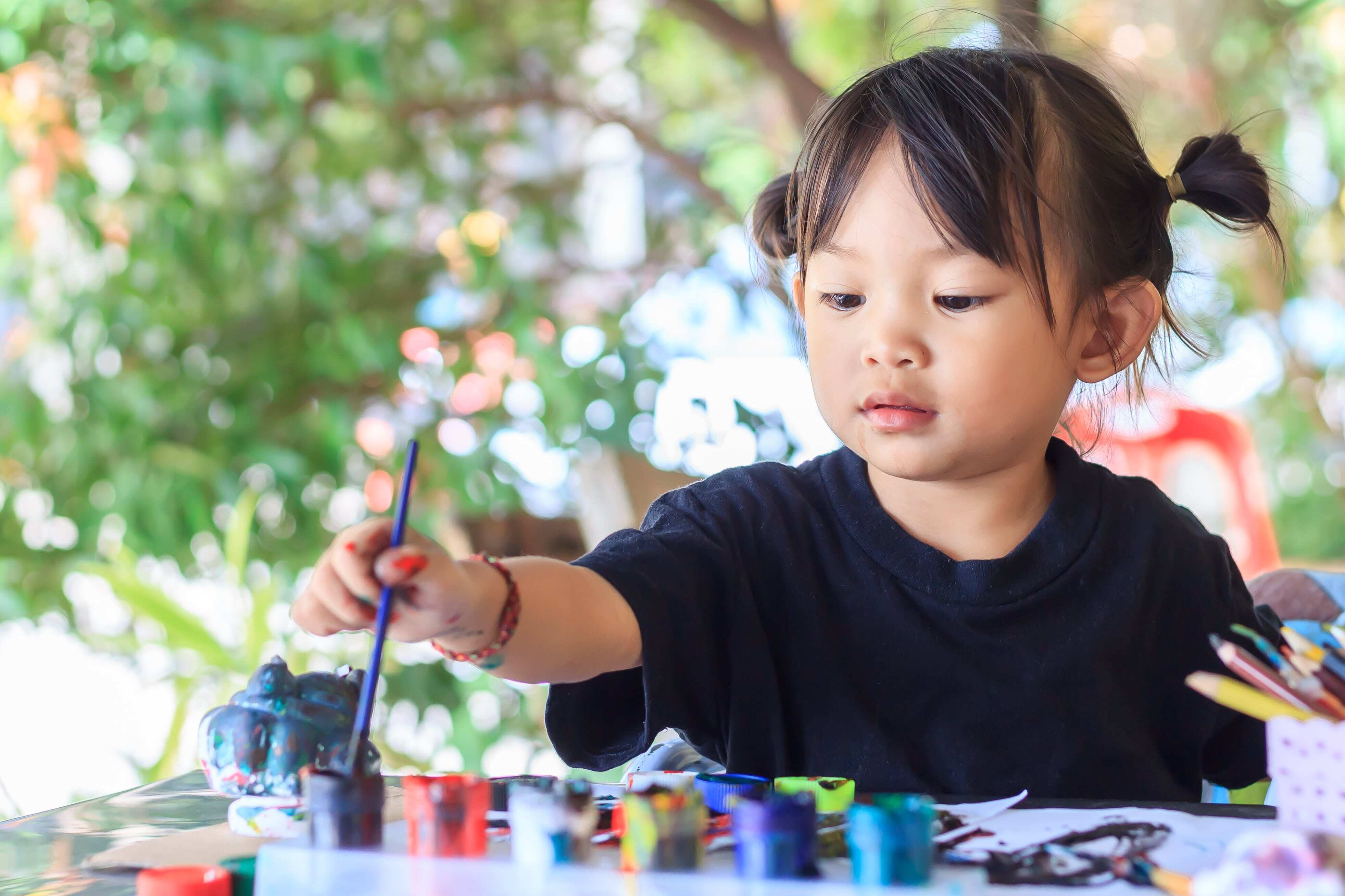 A young child sitting outside with a paint palette, creating art and learning essential skills. 