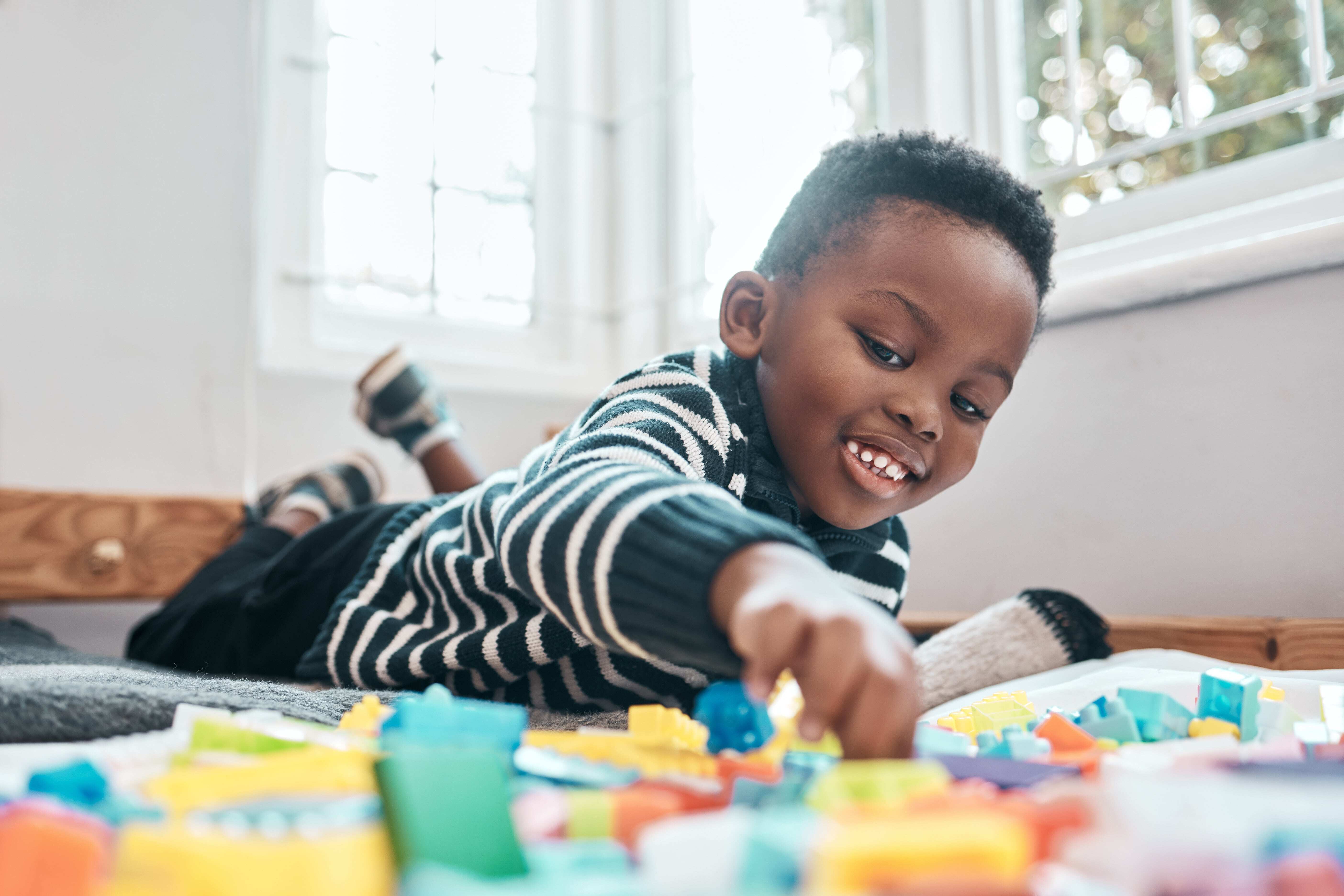 A toddler playing with his toys on the floor, practicing fine motor skills through play.