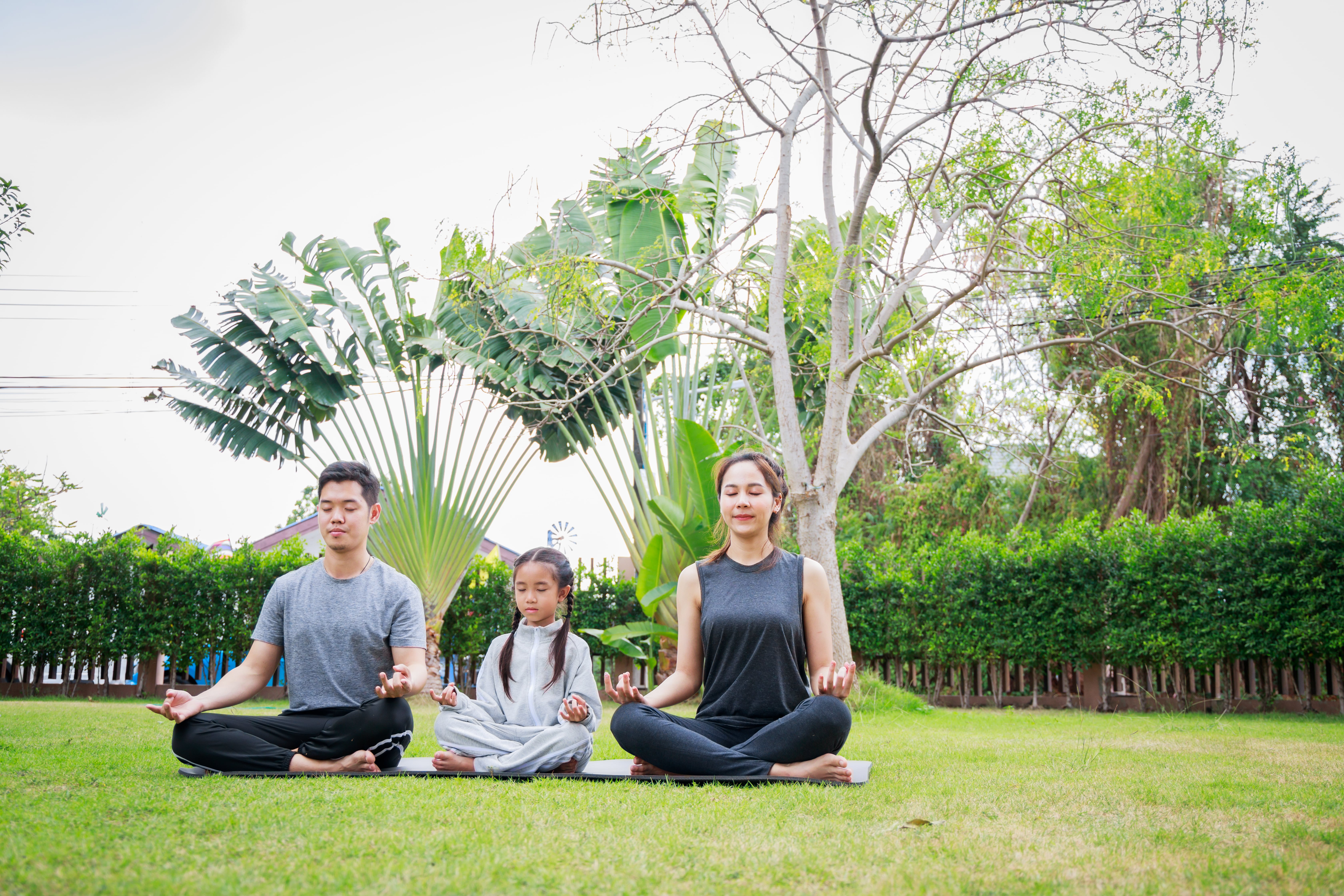 A family sitting together outside doing yoga as self-care for parents. 