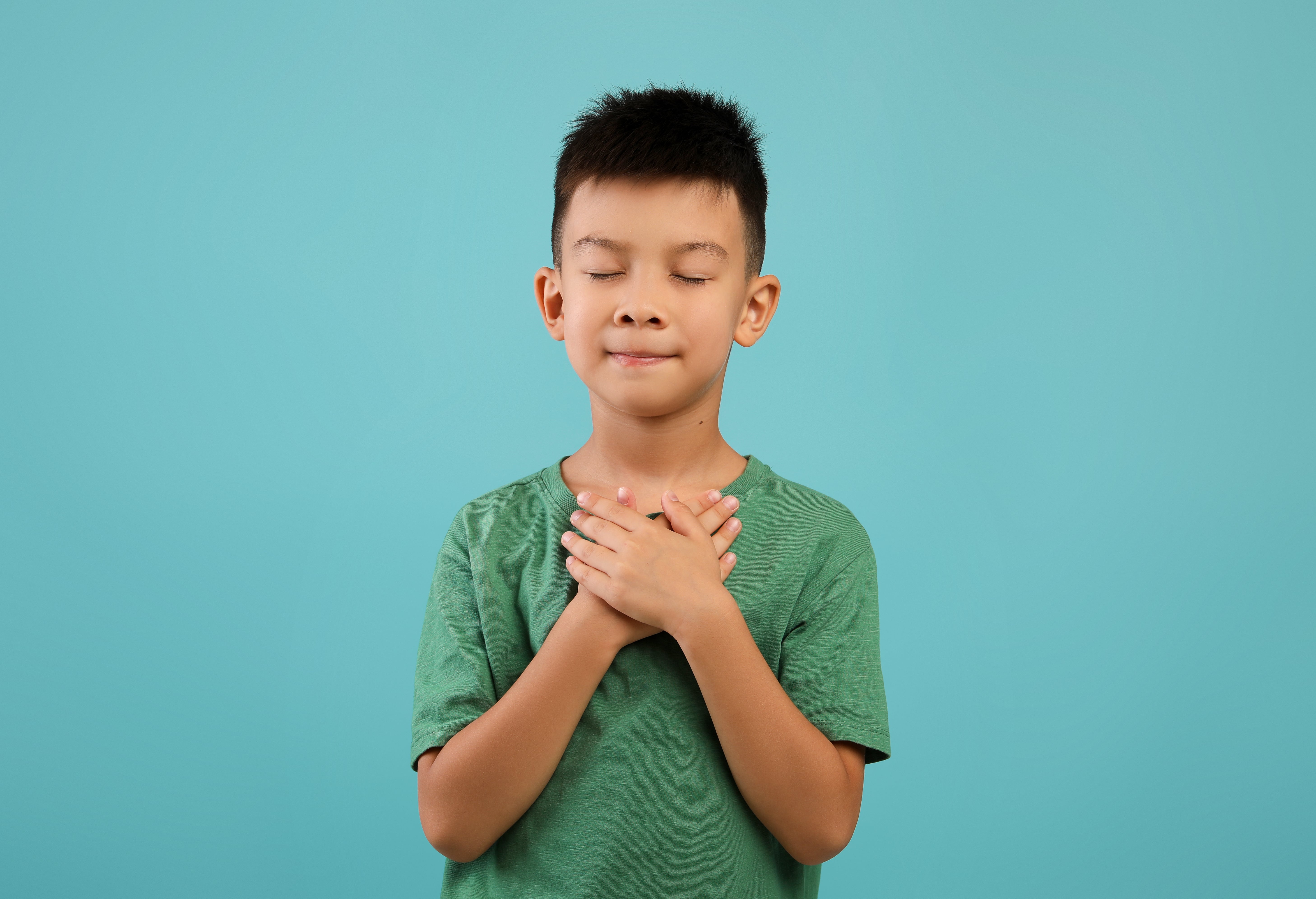 A young boy holding his hands to his heart practicing gratitude activities for kids. 