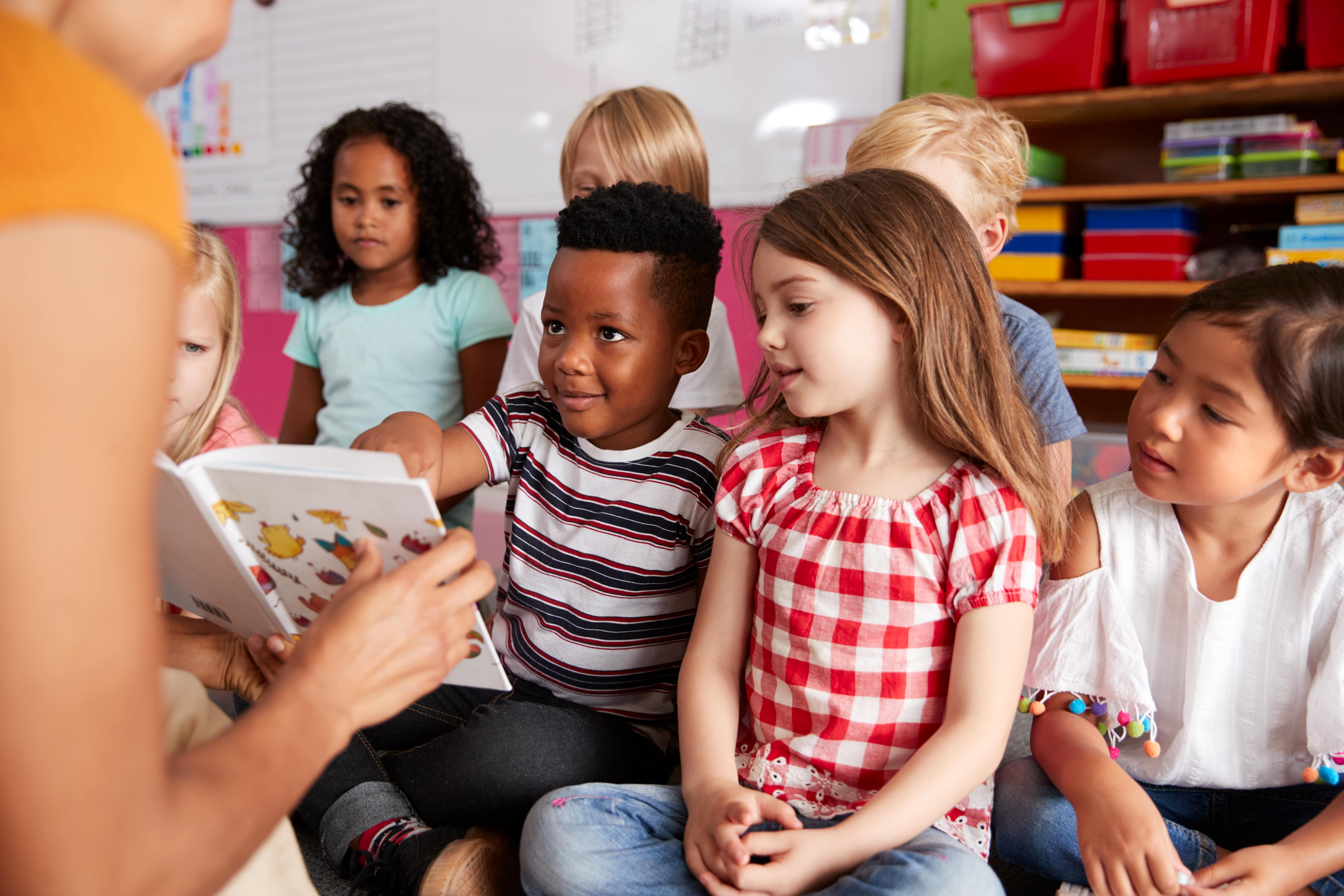 A group of children enjoying circle time at daycare reading a book with their educator. 