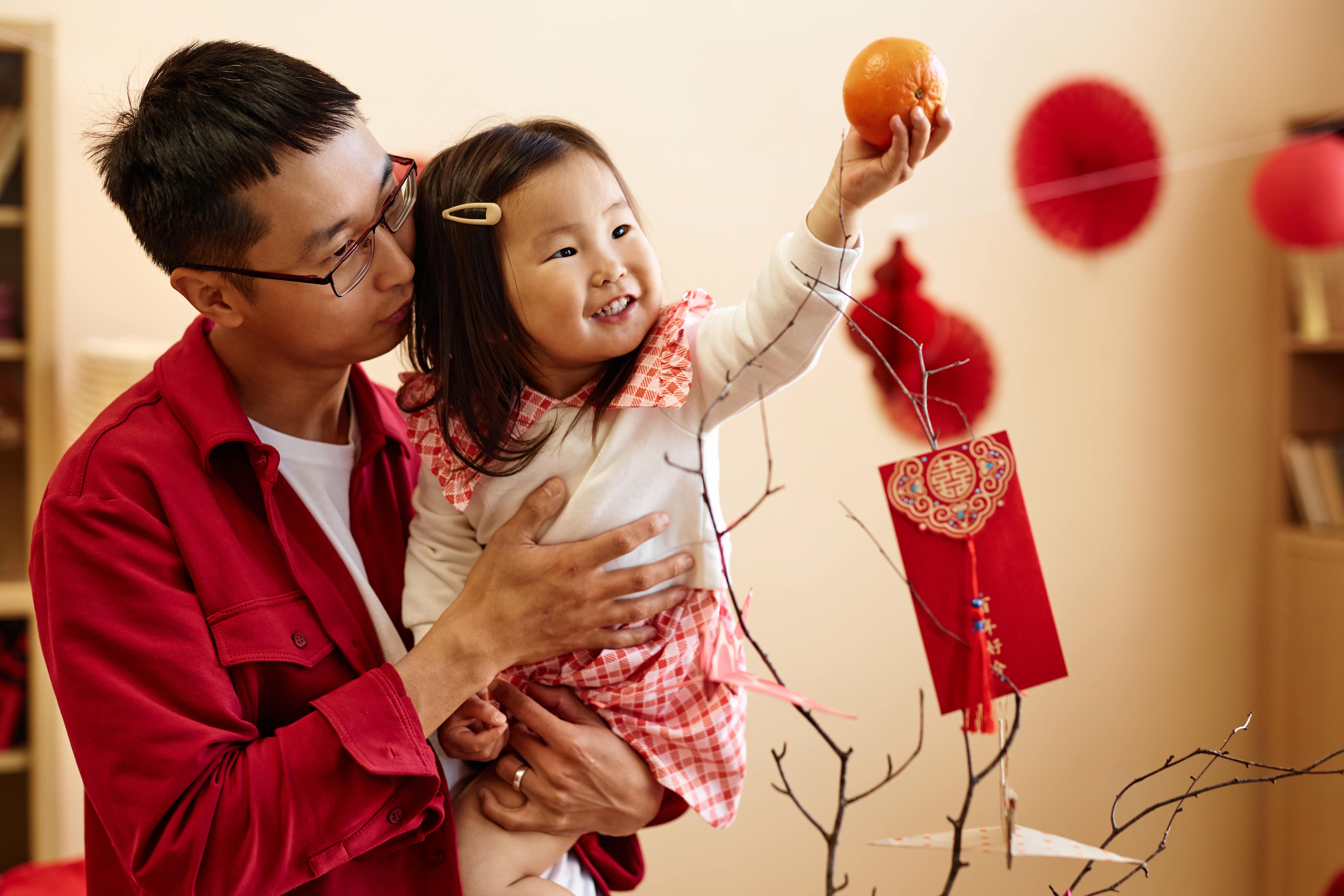 A young girl and her father hanging red envelopes, decorating and celebrating Lunar New Year with activities for kids.