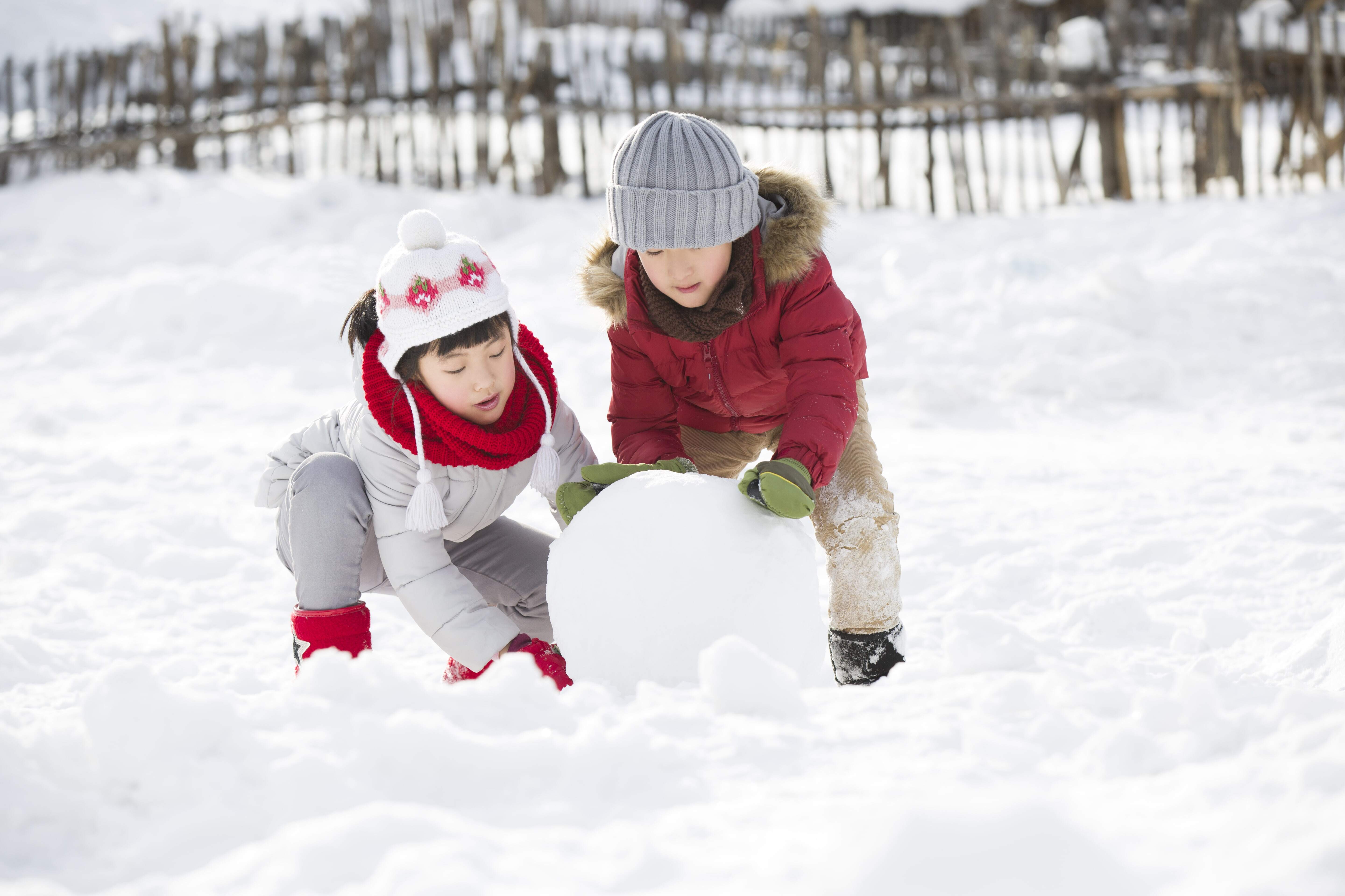 Two young children rolling a snowball together and having fun doing winter snow day activities for kids