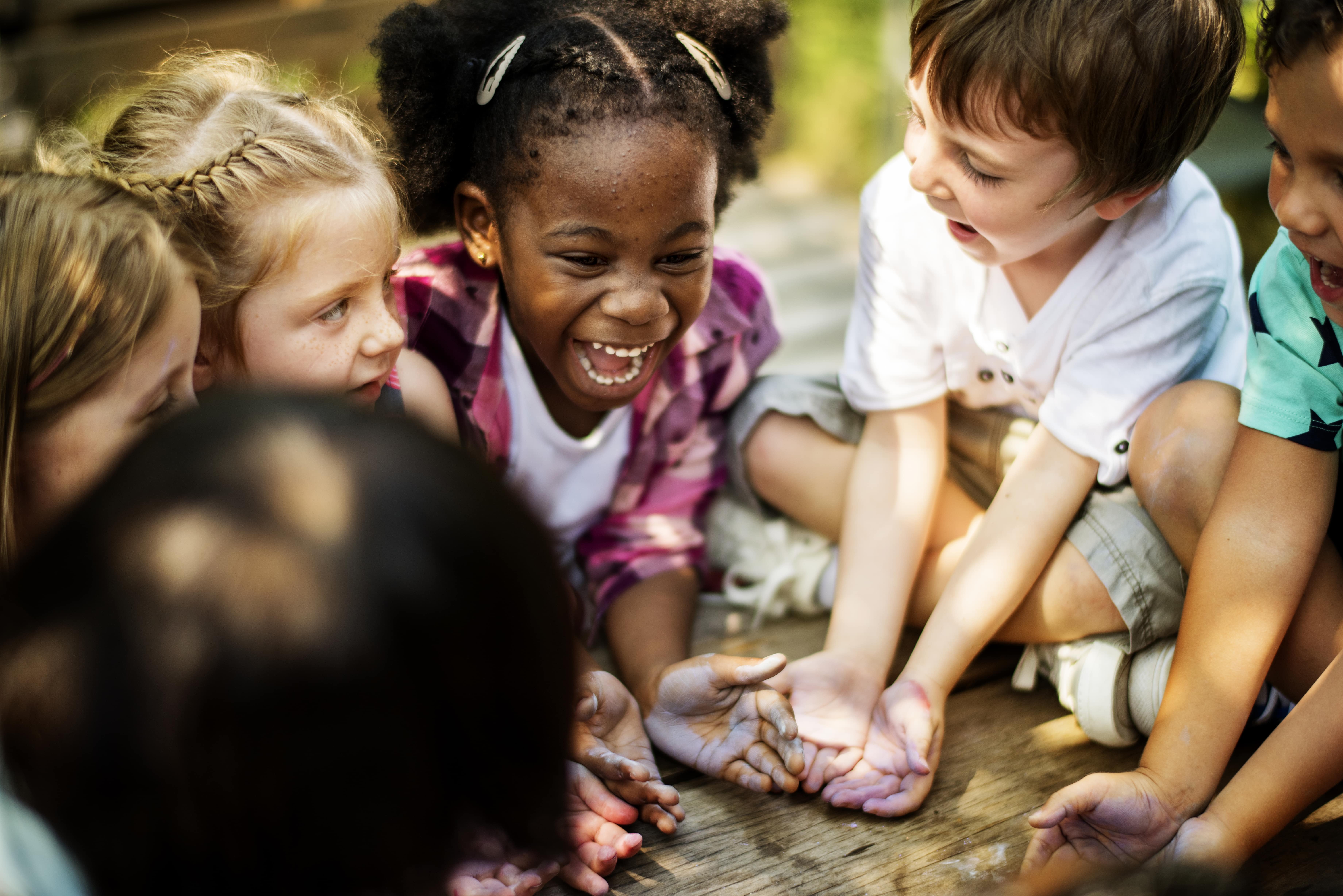 A group of young children playing and learning together outside, laughing and learning about environmental stewardship