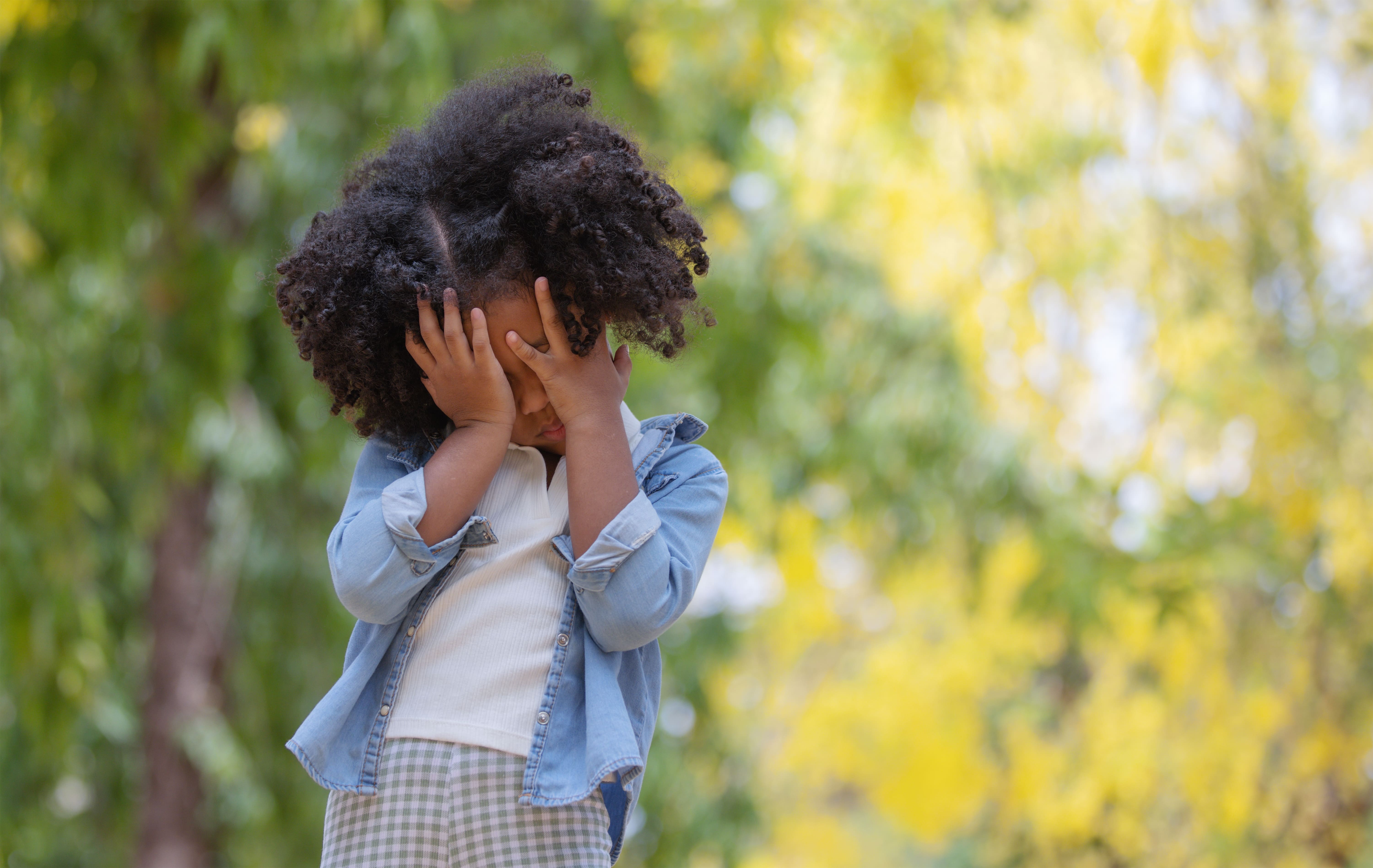 A young girl hiding behind her hands out of stress or fear. Try positive affirmations to support mental health.