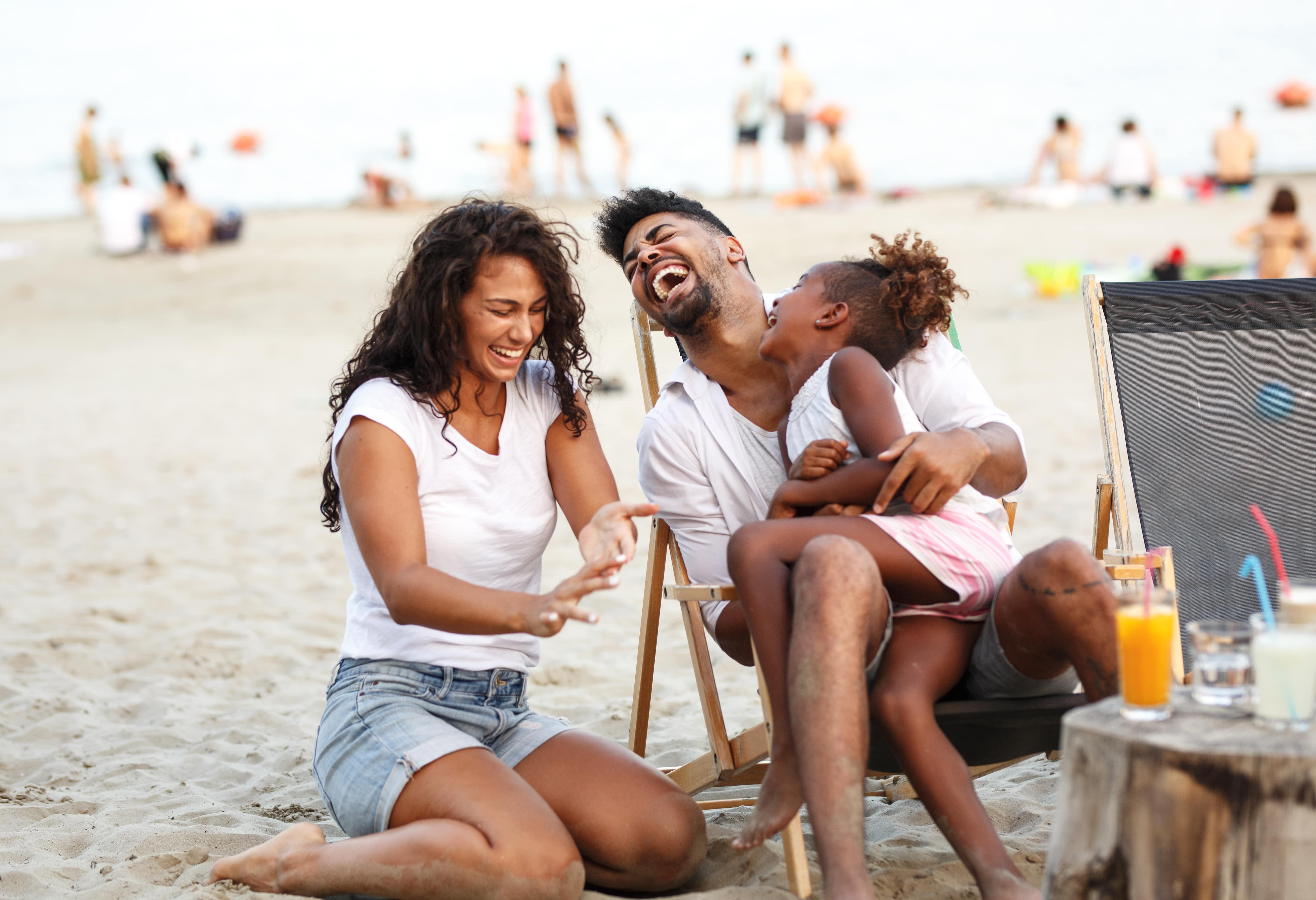 A young family smiling, laughing, and enjoying time together on the beach, learning to cultivate work-life balance this summer. 
