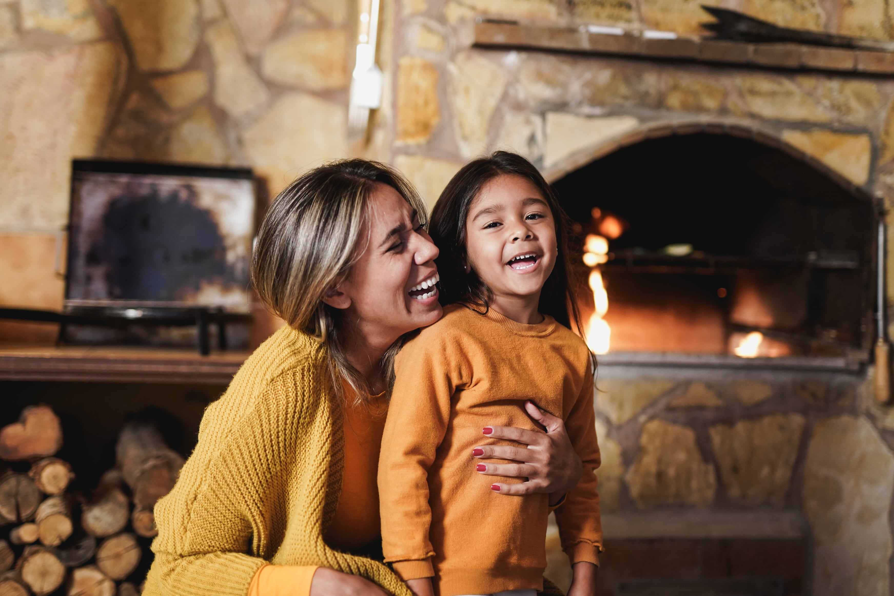 A mother hugging her daughter by the fireside. 