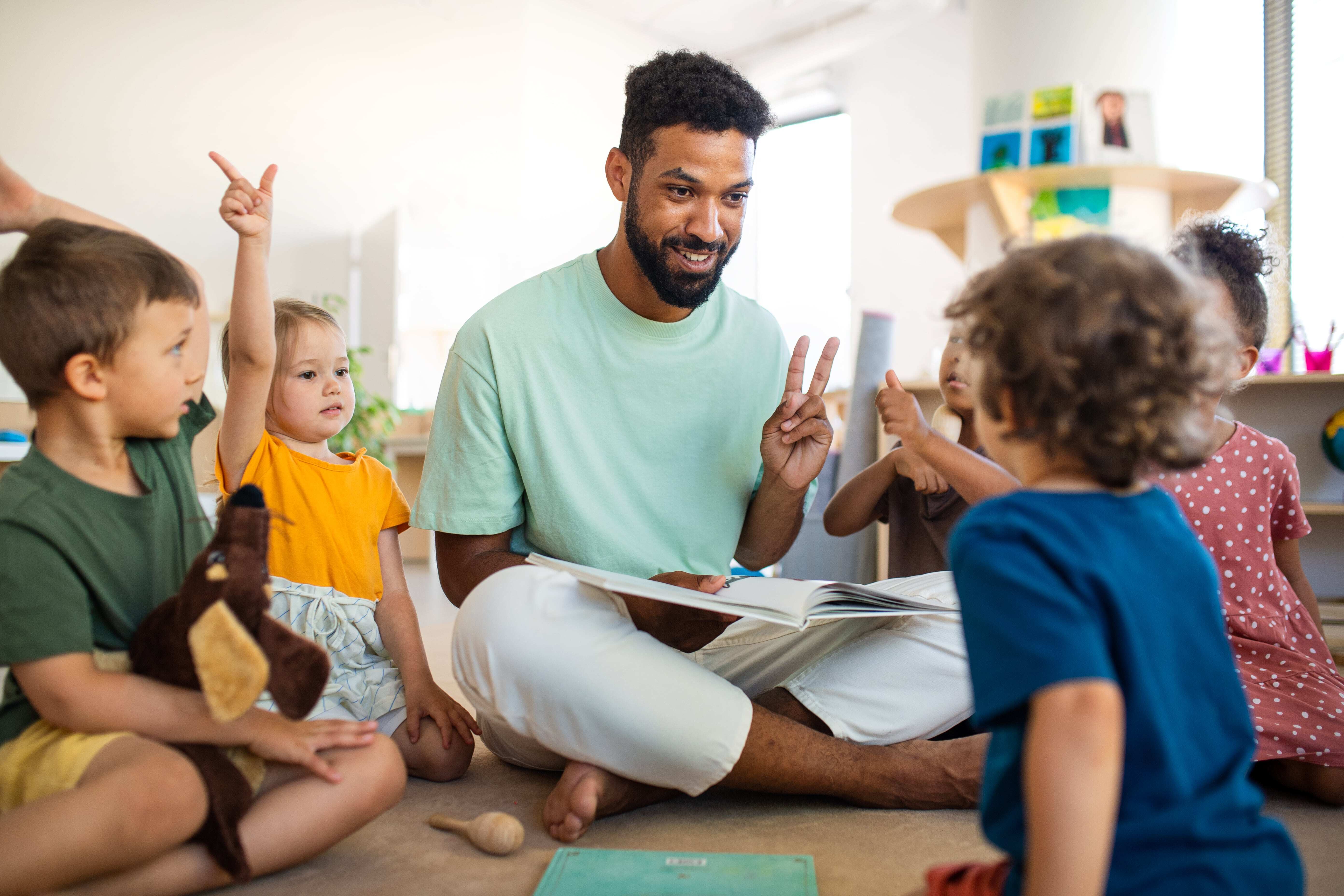 An educator sitting with his class reading a story and teaching the children about different emotions, helping them develop social emotional literacy