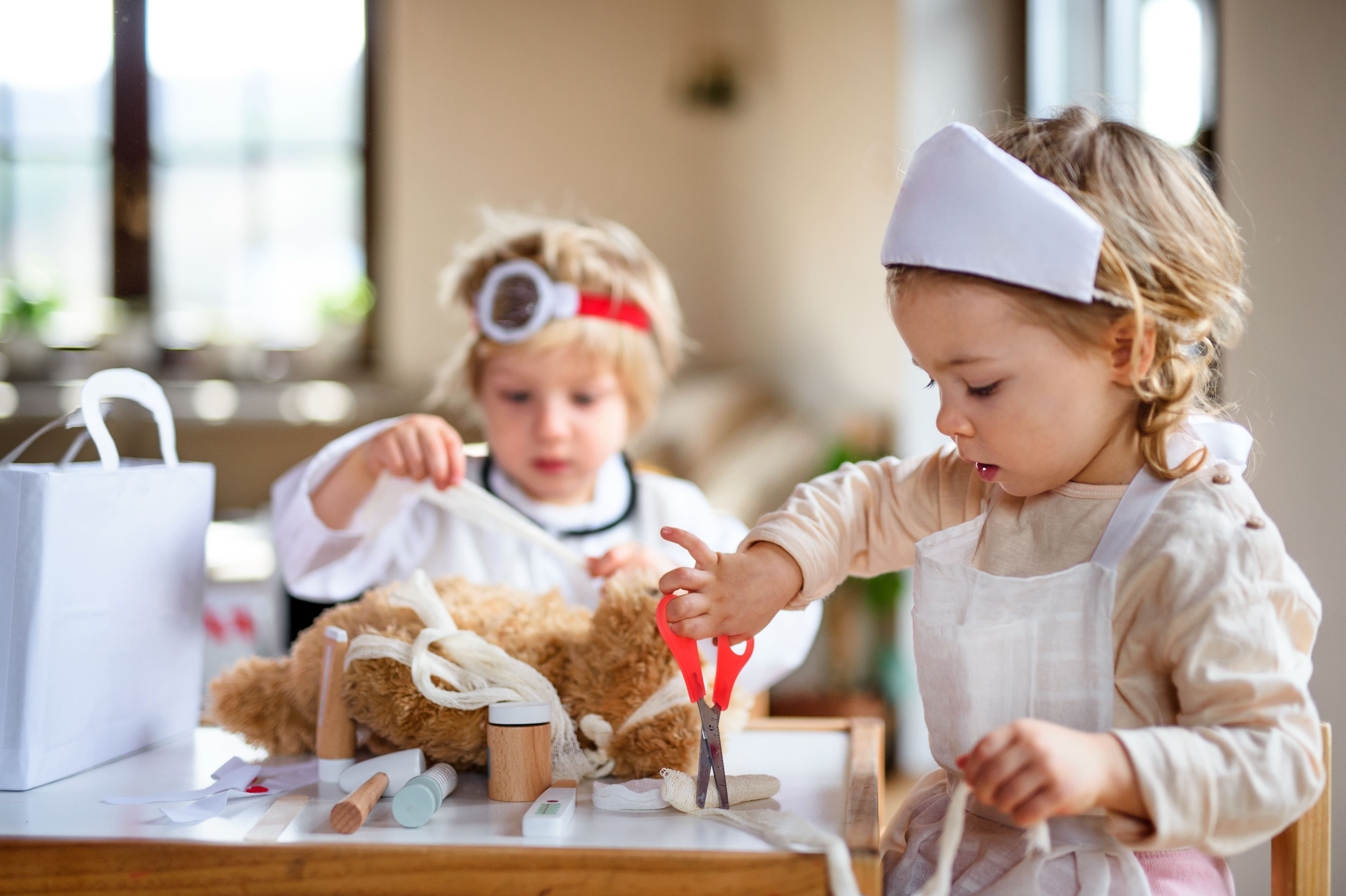 Two children in a BrightPath centre near you wearing doctor's hats and stethoscopes pretending to give care to a teddy bear as part of learning through play.